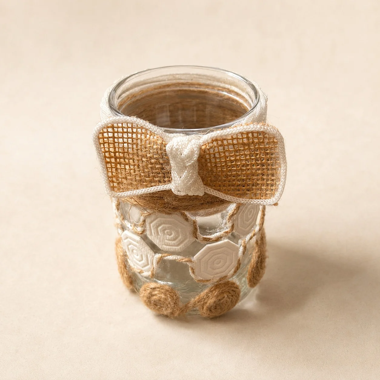 Glass jar decorated with cream and twine rosettes, topped with a large burlap bow trimmed in ivory.